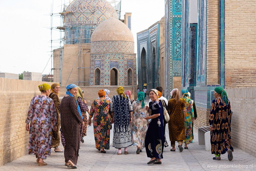 Oezbeekse vrouwen in kleurrijke jurken wandelen tussen de betegelde tombes in Samarkand